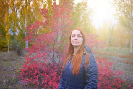 portrait of a life style woman with red hair in autumn against a background of colorful foliageの写真素材