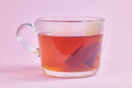 the tea bag is brewed in a transparent glass cup on a pink backgroundの写真素材