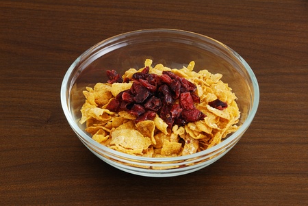 Cornflakes with dried cranberries in glass bowl on dark wooden table