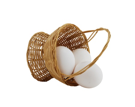 three white eggs spilled from straw interwoven basket isolated on white backgroundの写真素材