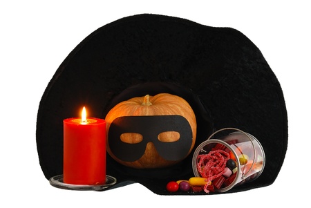 Halloween candies, burning orange candle and masqueraded pumpkin inside black witch hat isolated on white backgroundの写真素材