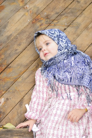 Portrait of the small beautiful girl in a dark blue scarf bent on a fenceの写真素材
