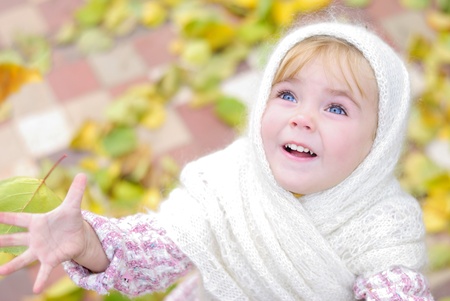 Portrait of the small beautiful girl in a white scarf in the autumnの写真素材