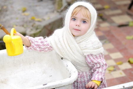 Portrait of the small beautiful girl in a white scarf with a watering canの写真素材