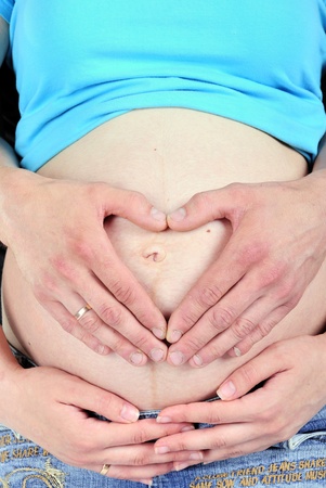 The stomach of the pregnant girl is embraced by hands of the husband in the form of heart の写真素材