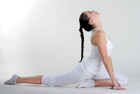 The young beautiful girl in white clothes is engaged in gymnastic exercises on a white backgroundの写真素材