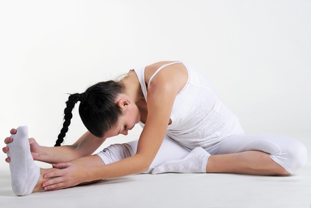 The young beautiful girl in white clothes is engaged in gymnastic exercises on a white backgroundの写真素材