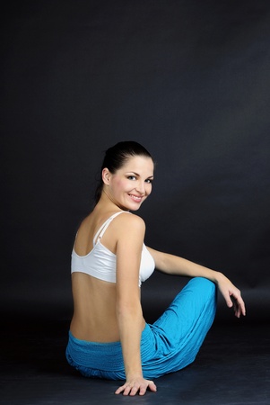 The young beautiful girl in bright clothes is engaged in gymnastic exercises on a gray backgroundの写真素材
