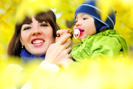 The small beautiful boy among yellow autumn leaves with mumの写真素材