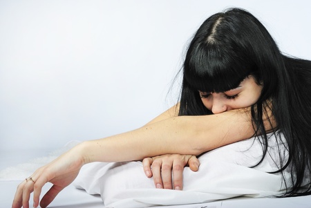 younger beautiful girl with black long hair in white bedの写真素材