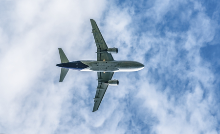 passenger jet flying in the cloudy sky under natural light bottom viewの写真素材