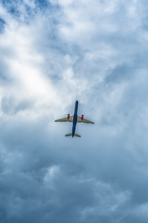 passenger jet flying in the cloudy sky under natural light bottom view