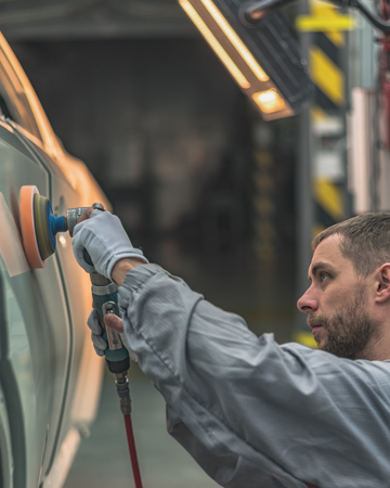 An employee of the car body painting shop polishes the painted surface with a pneumatic polishing...