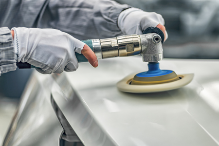 An employee of the car body painting shop polishes the painted surface with a pneumatic polishing...