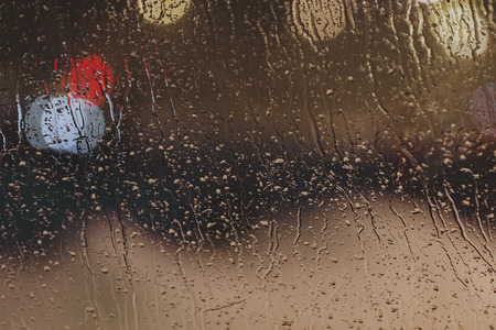 Drops and streams of water on the glass after the rain on a multicolored blurred backgroundの写真素材