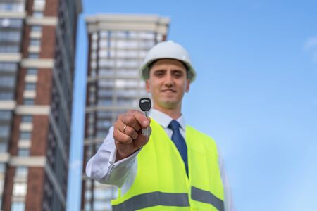 civil engineer in a white helmet on the background of construction, holds out the key. Natural lightの写真素材