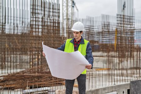 civil engineer in a white helmet looking documents on the background of construction, natural lightの写真素材