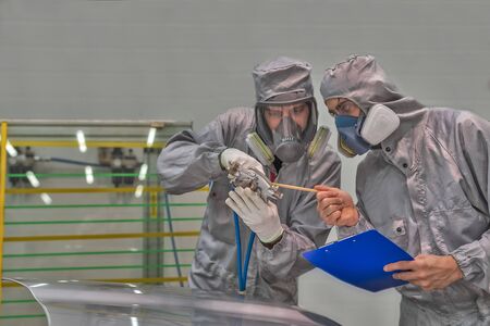 An employee of the paint shop of an automobile plant conducts training on painting body parts with a gun. Maintenance of working toolsの写真素材