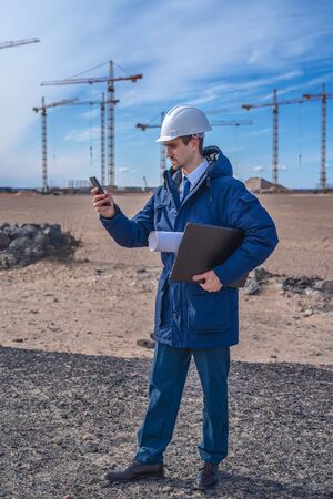 a civil engineer in a white helmet is talking on the phone in the background of construction. natural light.の写真素材