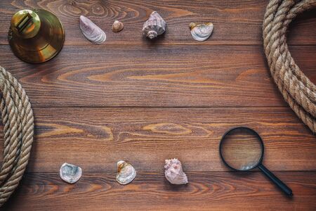 Shells, magnifying glass, bell and rope on dark brown wooden boards as background texture. Travel conceptの写真素材