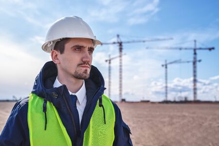 a civil engineer in a white helmet, winter jacket and yellow vest against the background of...