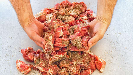 Pieces of raw meat in the hands of the cook on the gray table. Pork for baking.の写真素材