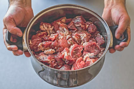 A pot full of chunks of raw meat in the hands of the cook. Pork for the grill.の写真素材