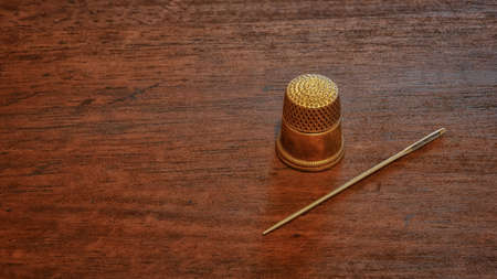 A sewing needle and an antique gold thimble. Geometric composition on a wooden table surface