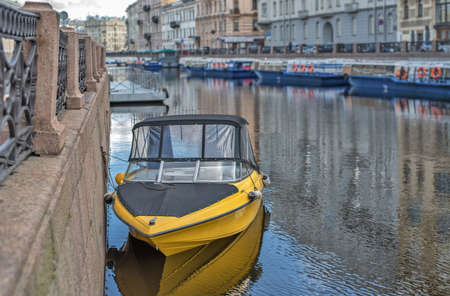 A yellow boat stands in the city channel against the background of a blurred city. Natural lightの写真素材
