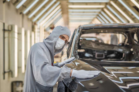 An employee of the paint shop of an automobile factory in a medical mask on his face checks the...