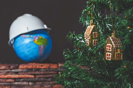 Christmas toy in the form of a house on the background of a globe in a construction helmet. Christmas tree. Greeting pictureの写真素材