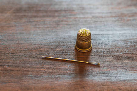A sewing needle and an antique gold thimble. Geometric composition on a wooden table surfaceの写真素材