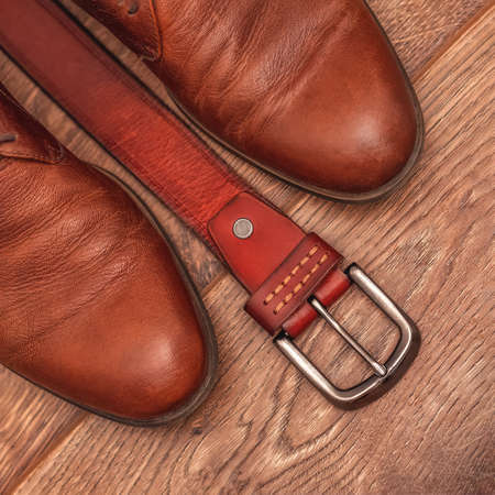 Classic men's brown leather shoes with a belt on a wooden background. Close upの写真素材