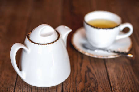 White ceramic teapot and a Cup of invigorating fresh fragrant tea on a brown wooden table. Afternoon tea.の写真素材