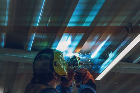 A welder wearing a yellow mask performs the work with a MIG-MAG welding machine.