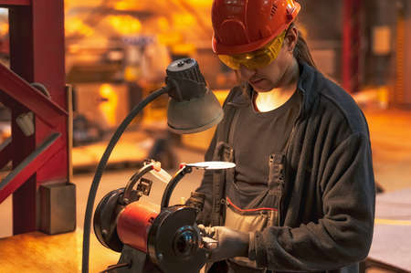 Close-up of the hands of a worker in black gloves working on a metal part on a red grinding machine