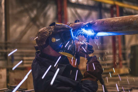 A welder wearing a protective mask performs the work with a MIG-MAG welding machine. Production of...