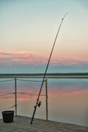 The bottom fishing rod stands with a stretched line against the background of the evening sky....