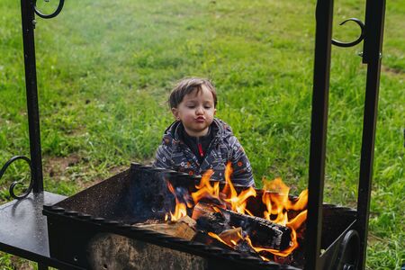 Little boy funny tries to fan the fire in the grillの写真素材