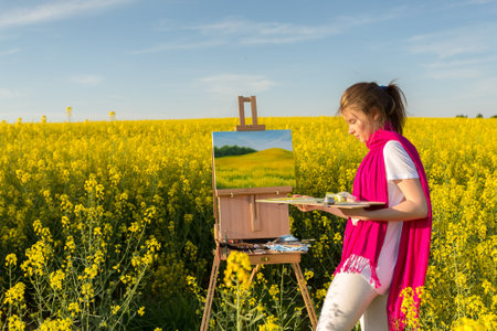 girl painter with an easel in a yellow rapeseed fieldの写真素材