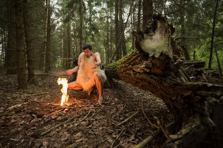 Caveman in animal skin kindles a fire in the forestの写真素材