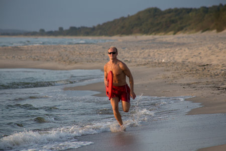 lifeguard on the beach with glasses, with a life buoy, wet sand and sea at sunsetの写真素材
