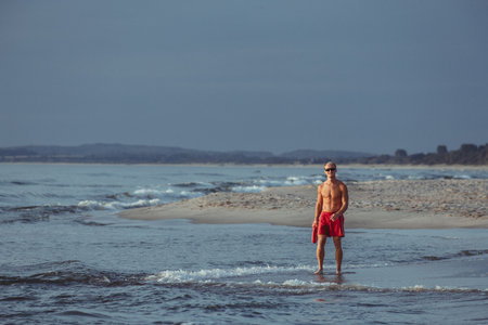 lifeguard on the beach with glasses, with a life buoy, wet sand and sea at sunsetの写真素材