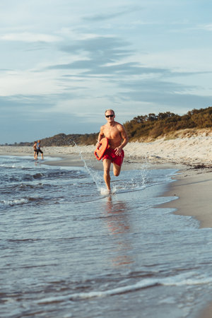 lifeguard on the beach with glasses, with a life buoy, wet sand and sea at sunsetの写真素材
