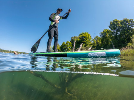 Man paddling on stand up paddle board on lake. Half underwater shot. SUP sportの写真素材