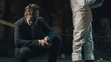 Detective inspecting area at crime scene at night as forensic experts collect evidence behind police tape next to headless body.の写真素材