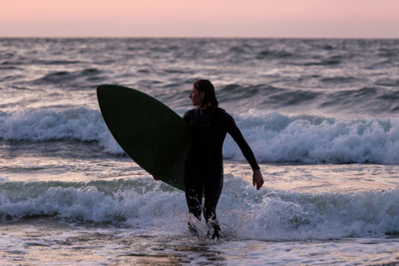 Surfer in a wetsuit enters the Baltic Sea with his board