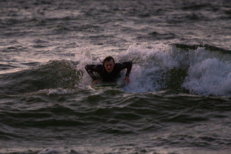 Surfer paddles out onto a small wave in the Baltic Sea