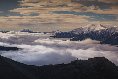 Medieval tower on mount above clouds, with snowy peaks in the background
