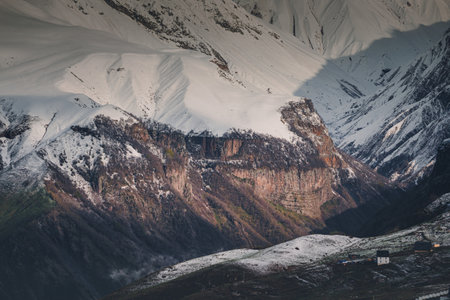 Gorge and several houses, a steep cliff and snowy mountains